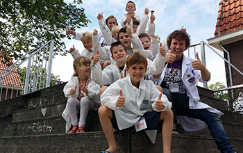 Kids in mad science lab coats and a mad scientist sitting on stairs with their thumbs up